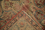 Folded antique Kerman rug detail, showing worn pile, red selvage, and curvilinear motifs.