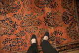 Feet on vintage Sarouk rug, dusty rose field, navy floral motifs, speckled abrash.