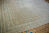 Distressed Mir Sarouk carpet corner: sand, ivory, sky blue banded borders and repeating boteh pattern.