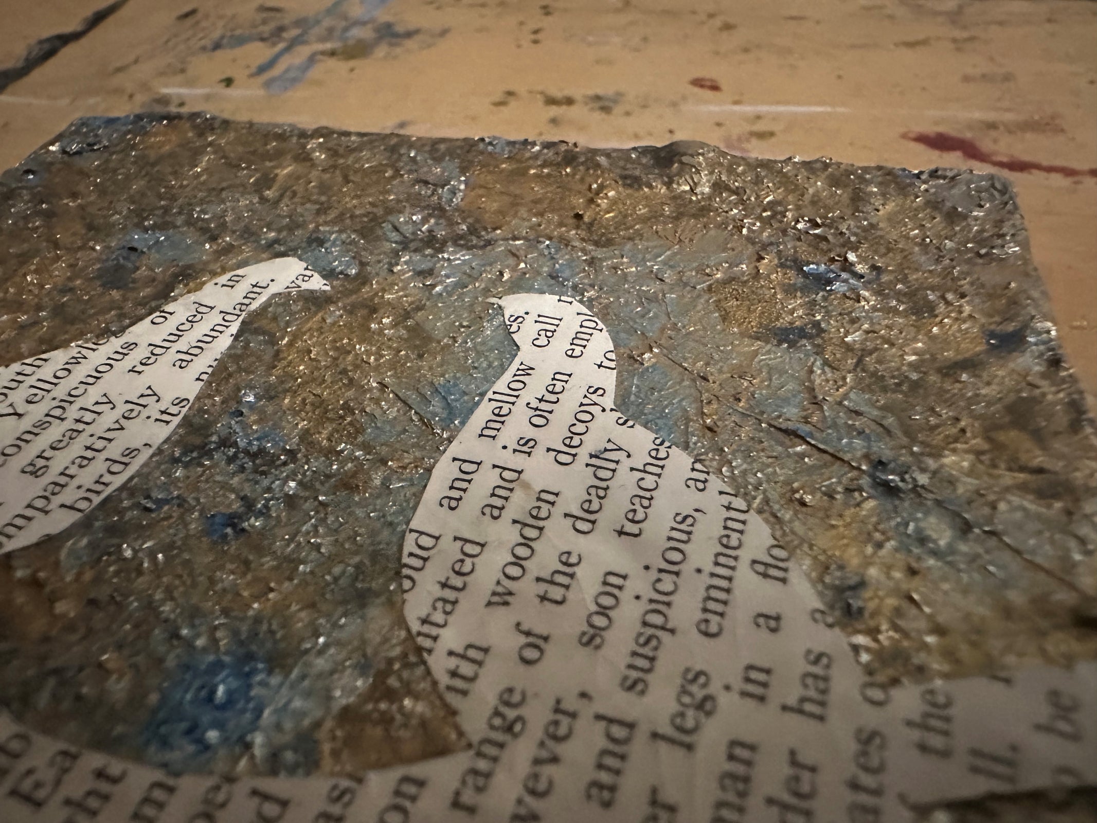 Detailed texture of "The Written Bird" art, with metallic silver leaf and vintage text bird shape.