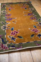 Angled detail of vintage Nichols Art Deco runner, gold field, green border, purple and pink stylized flowers.