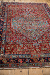 Bijar rug corner with navy blue and sky blue borders, pomegranate red Herati field, and white fringe.