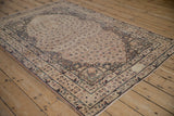 Distressed antique Kerman rug corner revealing worn ivory field and navy border with leopard print blossoms.
