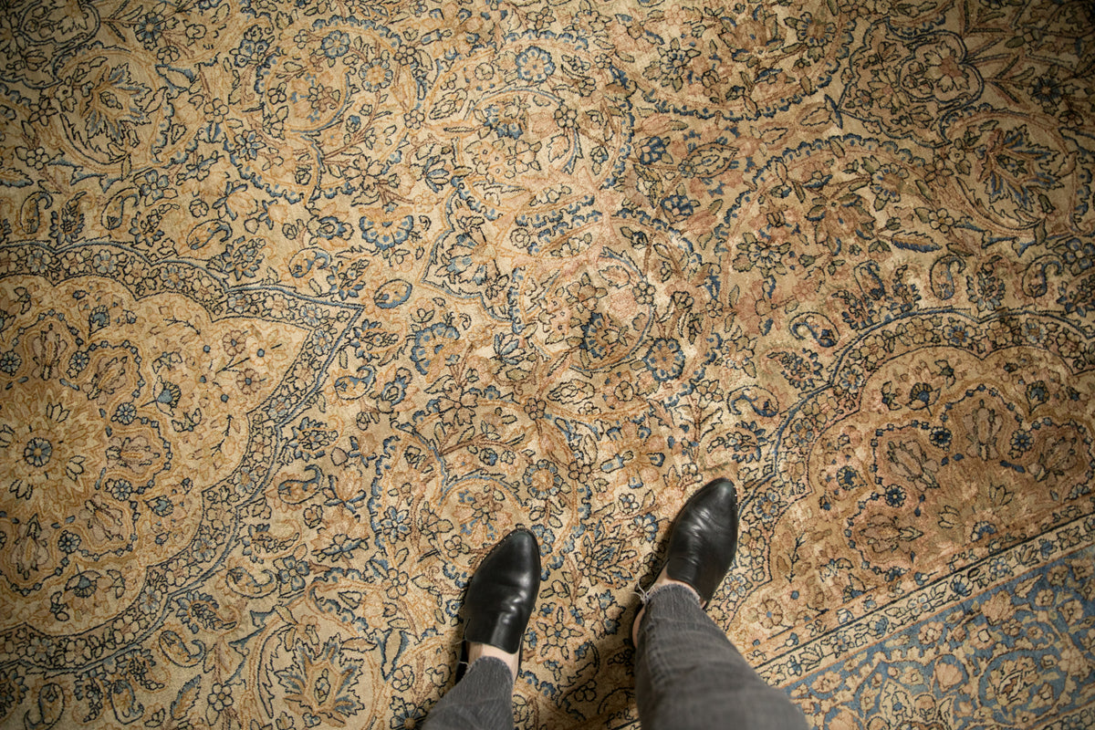 Vintage Kerman carpet's luxurious wool pile, intricate scrolled arabesque in gold, ivory, and denim blue.