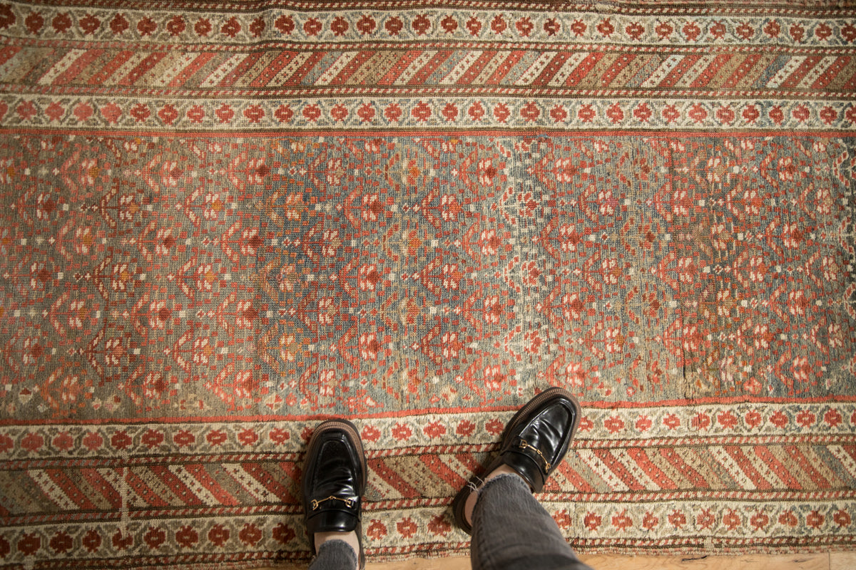Distressed Antique Kurdish runner features faded teal, rust plant motifs, and striped borders.