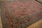 Antique Kerman carpet's blush field, showing abrashes, floral vines, and palmette border.
