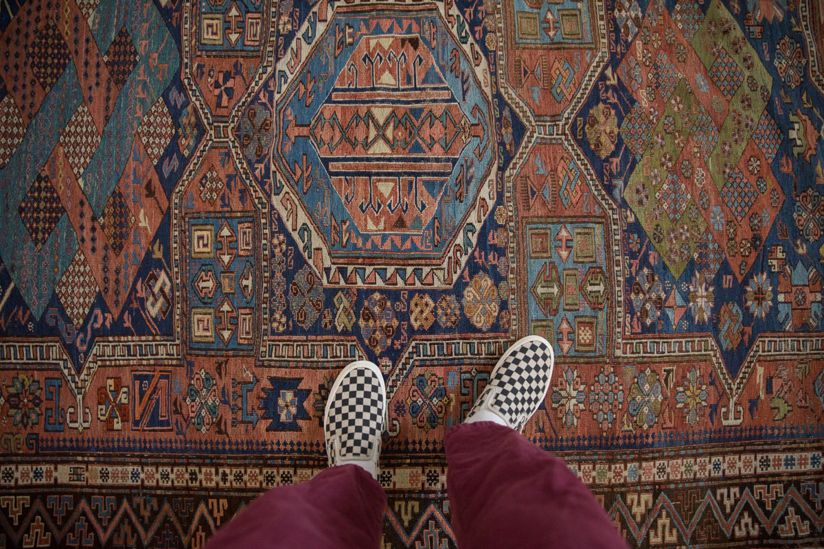 Antique Soumac rug with madder red field, blue geometric medallions, and tribal borders.