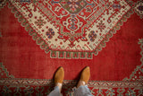 Hand-knotted texture of a distressed Oushak carpet, showing the geometric medallion against the cherry red field.