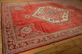 Angled view of a distressed Oushak carpet's geometric spandrels and ivory medallion on a cherry red field.