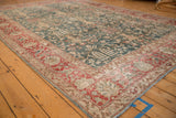 Angled view of a distressed Tabriz carpet showing its cherry red border and green floral field.