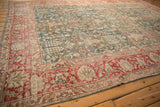 Corner detail of a distressed Persian Tabriz carpet highlighting the worn texture of its red border and green floral field.