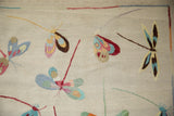 Close-up detail of the hand woven kilim showing colorful pictorial dragonflies on a beige surface.