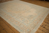 Angled view of a distressed Persian carpet highlighting its sand field and pale blue spandrels.