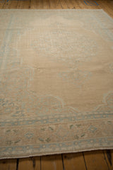 Angled view across the sandy open field of a distressed Persian rug, showing its soft, low-pile texture.