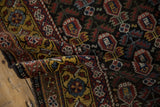 Folded vintage Qashqai rug contrasting the saffron border with dark chocolate repeating plant motifs.