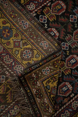 Folded corner of a vintage Qashqai runner reveals the saffron gold border and secured fringe.