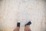 Distressed Afghani Oushak carpet showing worn texture, subtle palmette pattern, and a pair of sneakers.