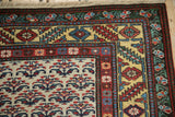 A vintage Persian rug's corner with a gold serrated leaf border framing an ivory shrub-patterned field.