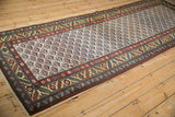 Angled view of a vintage Persian runner highlighting its goldish serrated leaf border and lattice field.