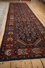 Angled view down the length of a vintage Hamadan runner with a traditional navy and red Herati pattern.
