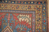 A close-up of the starburst blossom border on a vintage Persian Heriz rug in sand, blue, and red.