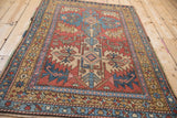 Vintage Persian Heriz rug with bird motifs and serrated leaves seen from a full angled view.