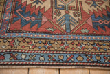 Hand-knotted starburst blossom border with red, blue, and sand tones on a vintage Heriz rug.