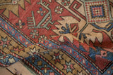 Curled corner of a vintage Heriz rug showing the short pile and starburst blossom border.