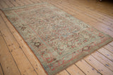 Distressed vintage Bijar rug viewed from a long angle, showing the allover Herati pattern and faded colors.