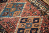 Madder red field with navy, camel diamond medallions and geometric pawn border detail.