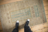 Vintage distressed Belouch rug with faded dusty teal, coffee tones, and geometric hook design.