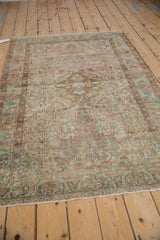 The overall distressed character and faded floral pattern of a vintage Sarouk rug viewed from an angle.