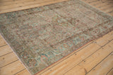 Angled perspective of a vintage Sarouk rug showing its distressed texture and faded floral design.