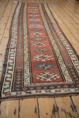 A long perspective view of an antique Caucasian runner with a repeating column of hook-and-latch medallions.