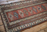 Angled view of an antique Caucasian runner, showing the intricate geometric borders and low, even wear.