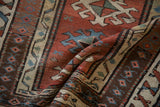 A soft fold in the antique Caucasian rug highlights its low-pile texture and rich, earthy palette.