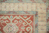 Distressed Caucasian rug corner with cherry red geometric wave motifs and visible wear.