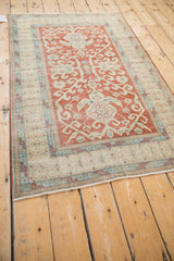 Decorative corner of distressed vintage Caucasian rug, showing blue wave motif and red plant border.