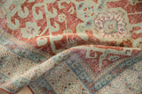 Textured fold of distressed vintage Caucasian rug, showing worn cherry red field and blue germinating plant border.