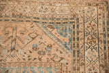 Distressed vintage Qashqai rug corner with time-softened ivory, blue, and brown geometric patterns.