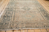 A long, angled view of the distressed Karaja rug shows its sandy field and worn geometric patterns.
