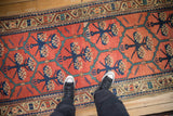 Person's view of an antique Persian runner with navy floral motifs on a tomato red ground.