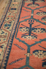 Low pile texture and knot heads on a Persian rug with dusty teal vines on a tomato red field.