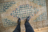Distressed Persian Mazlaghan rug with worn pile, dusty blue, ochre, and pink palmette design.