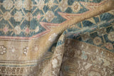 Folded distressed Mazlaghan rug showing faded blue palmette pattern and ochre border.