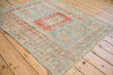 Angled view of a vintage Oushak rug with faded blue and red geometric patterns and a low, distressed pile.
