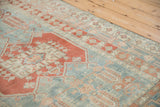 Angled view of the distressed Oushak's even wear, showcasing faded sky blue and madder red patterns.