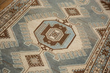 Angled close-up of a finned medallion and starburst border in dusty blue, ivory, and brown.