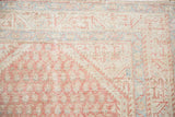 Corner of a distressed Persian rug showing low pile over blush and blue boteh motifs.