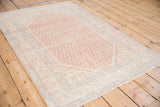 Angled view of the vintage Serbend rug's corner showing time-softened boteh patterns and a secure bound edge.